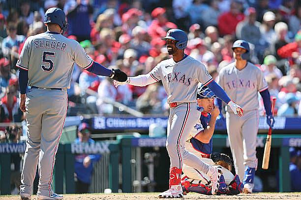 PHILADELPHIA, PENNSYLVANIA – MARCH 29: Andrew McCutchen #4 of the Texas Rangers is greeted at home plate by Corey Seager #5…