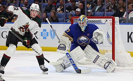 Dec 11, 2023; Buffalo, New York, USA;  Arizona Coyotes center Logan Cooley (92) and Buffalo Sabres goaltender Devon Levi (27) look for the puck during the first period at KeyBank Center. Mandatory Credit: Timothy T. Ludwig-USA TODAY Sports
