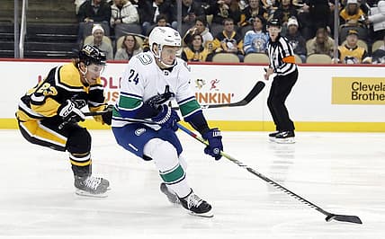 Jan 10, 2023; Pittsburgh, Pennsylvania, USA;  Vancouver Canucks defenseman Travis Dermott (24) moves the puck against Pittsburgh Penguins left wing Brock McGinn (23) during the first period at PPG Paints Arena. The Penguins won 5-4. Mandatory Credit: Charles LeClaire-USA TODAY Sports