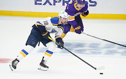 Mar 17, 2021; Los Angeles, California, USA; St. Louis Blues left wing Zach Sanford (12) moves the puck down the ice as Los Angeles Kings left wing Carl Grundstrom (91) gives chase during the first period at Staples Center. Mandatory Credit: Robert Hanashiro-USA TODAY Sports