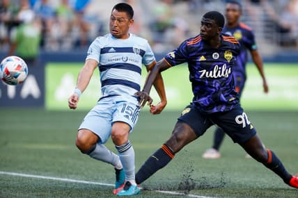 Jul 25, 2021; Seattle, Washington, USA; Sporting Kansas City midfielder Roger Espinoza (15) takes a shot ahead of Seattle Sounders FC defender Abdoulaye Cissoko (92) during the first half at Lumen Field. Mandatory Credit: Jennifer Buchanan-USA TODAY Sports