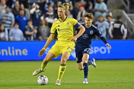 Apr 9, 2022; Kansas City, Kansas, USA; Nashville SC defender Walker Zimmerman (25) passes the ball while defended by Sporting Kansas City midfielder Marinos Tzionis (27) during the second half at Children's Mercy Park. Mandatory Credit: Peter Aiken-USA TODAY Sports