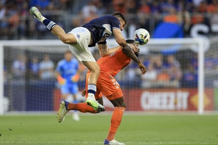 Jul 13, 2022; Cincinnati, Ohio, USA; Vancouver Whitecaps forward Lucas Cavallini (top) attempts to play the ball against FC Cincinnati defender Tyler Blackett (24) in the first half at TQL Stadium. Mandatory Credit: Aaron Doster-USA TODAY Sports