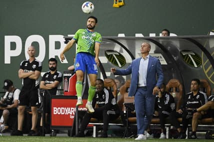 Aug 26, 2022; Portland, Oregon, USA; Seattle Sounders midfielder Alex Roldan (16) heads the ball during the first half next to Portland Timbers head coach Giovanni Savarese at Providence Park. The Timbers won 2-1. Mandatory Credit: Troy Wayrynen-USA TODAY Sports