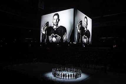 Oct 30, 2023; Pittsburgh, Pennsylvania, USA;  Members of the Anaheim Ducks and the Pittsburgh Penguins stand at center ice for a moment of silence at the PPG Paints Arena to honor former Penguin forward Adam Johnson (on scoreboard) who was tragically killed in a hockey related accident in Europe. Mandatory Credit: Charles LeClaire-USA TODAY Sports