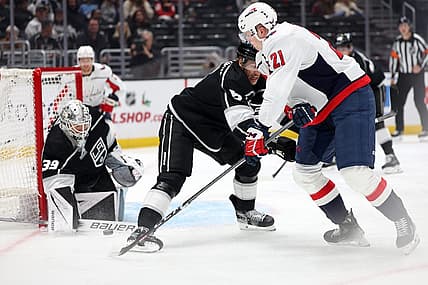 Nov 29, 2023; Los Angeles, California, USA; Washington Capitals center Aliaksei Protas (21) shoots the puck as Los Angeles Kings defenseman Andreas Englund (5) defends and goaltender Cam Talbot (39) protects the goal during the first period at Crypto.com Arena. Mandatory Credit: Kiyoshi Mio-USA TODAY Sports.