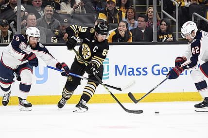 Dec 3, 2023; Boston, Massachusetts, USA; Boston Bruins left wing Brad Marchand (63) tries to control the puck between Columbus Blue Jackets defenseman Ivan Provorov (9) and center Alexandre Texier (42) during the first period at TD Garden. Mandatory Credit: Bob DeChiara-USA TODAY Sports