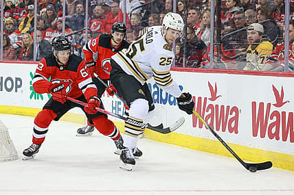 Dec 13, 2023; Newark, New Jersey, USA; Boston Bruins defenseman Brandon Carlo (25) skates with the puck as New Jersey Devils left wing Jesper Bratt (63) and center Nico Hischier (13) defend during the first period at Prudential Center. Mandatory Credit: Vincent Carchietta-USA TODAY Sports