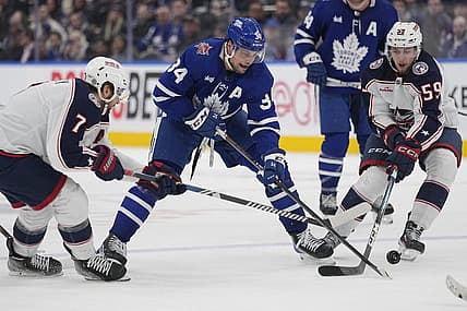 Dec 14, 2023; Toronto, Ontario, CAN; Toronto Maple Leafs forward Auston Matthews (34) battles for th epuck with Columbus Blue Jackets forward Sean Kuraly (7) and Columbus Blue Jackets forward Yegor Chinakhov (59) during the third period at Scotiabank Arena. Mandatory Credit: John E. Sokolowski-USA TODAY Sports