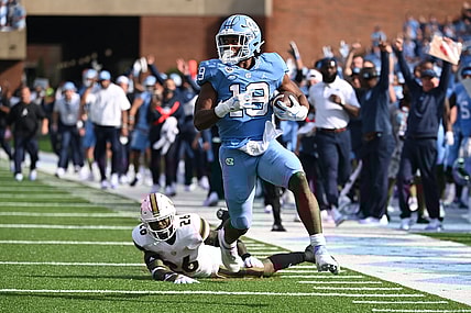 Oct 16, 2021; Chapel Hill, North Carolina, USA;  North Carolina Tar Heels running back Ty Chandler (19) runs for a touchdown as Miami Hurricanes safety Gurvan Hall Jr. (26) defends in the first quarter at Kenan Memorial Stadium. Mandatory Credit: Bob Donnan-USA TODAY Sports