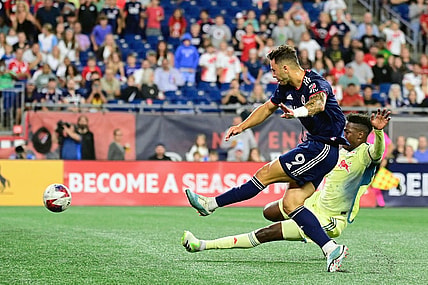 Aug 30, 2023; Foxborough, Massachusetts, USA; New England Revolution attacker Giacomo Vrioni (9) scores a goal as New York Red Bulls defender Hassan Ndam (98) slides to defend the shot during the first half at Gillette Stadium. Mandatory Credit: Eric Canha-USA TODAY Sports