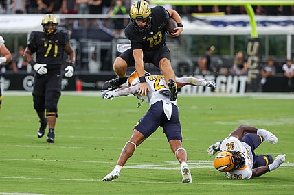Aug 31, 2023; Orlando, Florida, USA; UCF Knights quarterback John Rhys Plumlee (10) jumps over Kent State Golden Flashes safety Bryce Sheppert (27) during the first quarter at FBC Mortgage Stadium. Mandatory Credit: Mike Watters-USA TODAY Sports battle for the ball