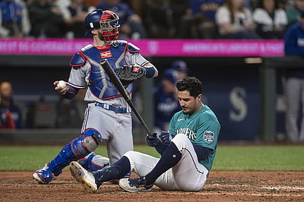 Sep 30, 2023; Seattle, Washington, USA; Seattle Mariners second baseman Josh Rojas (4) sits on the ground after dodging a pitch during the fifth inning at T-Mobile Park. At right is Texas Rangers catcher Jonah Heim (28). Mandatory Credit: Stephen Brashear-USA TODAY Sports
