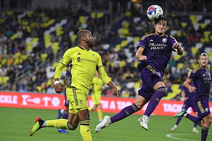 Oct 4, 2023; Nashville, Tennessee, USA; Orlando City defender Rodrigo Schlegel (15) heads the ball against Nashville SC forward Teal Bunbury (12) during the second half at Geodis Park. Mandatory Credit: Christopher Hanewinckel-USA TODAY Sports