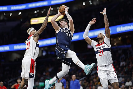 Nov 15, 2023; Washington, District of Columbia, USA; Dallas Mavericks guard Luka Doncic (77) leaps to pass the ball as Washington Wizards forward Kyle Kuzma (33) and Wizards center Daniel Gafford (21) defend in the first quarter at Capital One Arena. Mandatory Credit: Geoff Burke-USA TODAY Sports