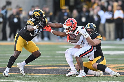 Nov 18, 2023; Iowa City, Iowa, USA; Illinois Fighting Illini running back Reggie Love III (23) is tackled by Iowa Hawkeyes defensive lineman Logan Lee (85) and linebacker Jay Higgins (34) during the second quarter at Kinnick Stadium. Mandatory Credit: Jeffrey Becker-USA TODAY Sports