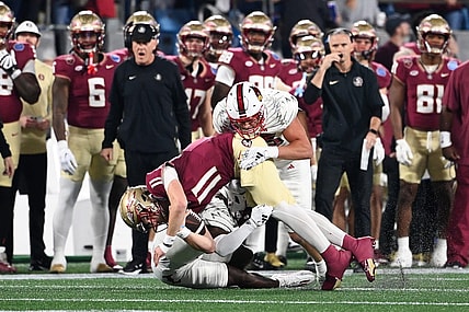 Dec 2, 2023; Charlotte, NC, USA; Florida State Seminoles quarterback Brock Glenn (11) is tackled by Louisville Cardinals defensive lineman Mason Reiger (95) and defensive back Quincy Riley (3) as he runs the ball in the second quarter at Bank of America Stadium. Mandatory Credit: Bob Donnan-USA TODAY Sports