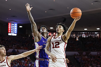 Feb 17, 2024; Norman, Oklahoma, USA; Oklahoma Sooners guard Milos Uzan (12) goes up for a basket beside Kansas Jayhawks forward K.J. Adams Jr. (24) during the second half at Lloyd Noble Center. Mandatory Credit: Alonzo Adams-USA TODAY Sports