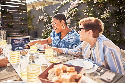 Two Girlfriends Watching Sling TV On Their Tablet While Eating On Their Patio