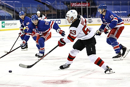 Feb 16, 2021; New York, New York, USA;  Jesper Bratt #63 of the New Jersey Devils takes a shot as Kevin Rooney #17 and Julien Gauthier #12 of the New York Rangers defend during the first period at Madison Square Garden. Mandatory Credit:  Elsa/POOL PHOTOS-USA TODAY Sports