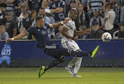 Apr 23, 2022; Kansas City, Kansas, USA;  Sporting Kansas City defender Kortne Ford (12) clears the ball away from Columbus Crew midfielder Darlington Nagbe (6) during the first half at Children's Mercy Park. Mandatory Credit: Peter Aiken-USA TODAY Sports