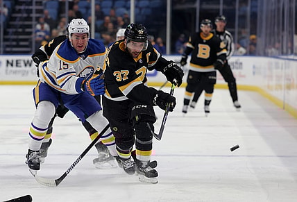 Oct 22, 2021; Buffalo, New York, USA;  Buffalo Sabres left wing John Hayden (15) tries to defend as Boston Bruins center Patrice Bergeron (37) shoots the puck along the boards during the first period at KeyBank Center. Mandatory Credit: Timothy T. Ludwig-USA TODAY Sports