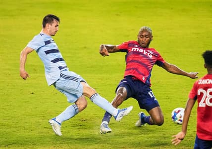 May 10, 2022; Kansas City, Kansas, USA; Sporting Kansas City forward Nikola Vujnovic (19) scores a goal against FC Dallas defender Nkosi Tafari (17) during the second half at Children's Mercy Park. Mandatory Credit: Jay Biggerstaff-USA TODAY Sports