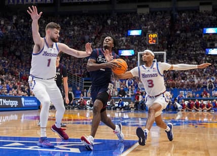 Dec 1, 2023; Lawrence, Kansas, USA; Connecticut Huskies guard Tristen Newton (2) drives against Kansas Jayhawks center Hunter Dickinson (1) and guard Dajuan Harris Jr. (3) during the first half at Allen Fieldhouse. Mandatory Credit: Jay Biggerstaff-USA TODAY Sports