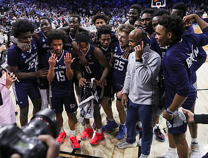 Mar 25, 2022; Philadelphia, PA, USA; Saint Peter's players celebrate around head coach Shaheen Holloway as he does a television interview after the Peacocks' 67-64 win against Purdue to advance to the Elite Eight in the NCAA tournament at the Wells Fargo Center in Philadelphia, March 25, 2022. Mandatory Credit: William Bretzger-USA TODAY NETWORK
