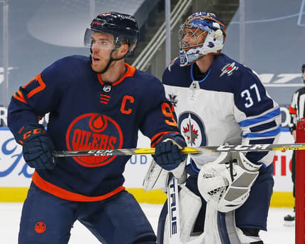Mar 20, 2021; Edmonton, Alberta, CAN; Edmonton Oilers forward Connor McDavid (97) looks for a puck in front of Winnipeg Jets goaltender Connor Hellebuyck (37) during the first period at Rogers Place. Mandatory Credit: Perry Nelson-USA TODAY Sports