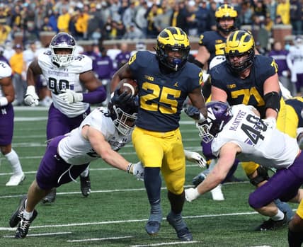 Michigan Wolverines running back Hassan Haskins (25) runs by Northwestern Wildcats defensive back Trent Carrington (20) and linebacker Peter McIntyre (40) during second half action Saturday, Oct. 23, 2021 at Michigan Stadium.

Mich Nw