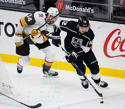 Mar 19, 2021; Los Angeles, California, USA; Los Angeles Kings center Trevor Moore (12) moves the puck away from Vegas Golden Knights defenseman Nicolas Hague (14) during the second period at Staples Center. Mandatory Credit: Robert Hanashiro-USA TODAY Sports