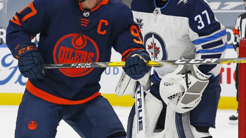 Mar 20, 2021; Edmonton, Alberta, CAN; Edmonton Oilers forward Connor McDavid (97) looks for a puck in front of Winnipeg Jets goaltender Connor Hellebuyck (37) during the first period at Rogers Place. Mandatory Credit: Perry Nelson-USA TODAY Sports