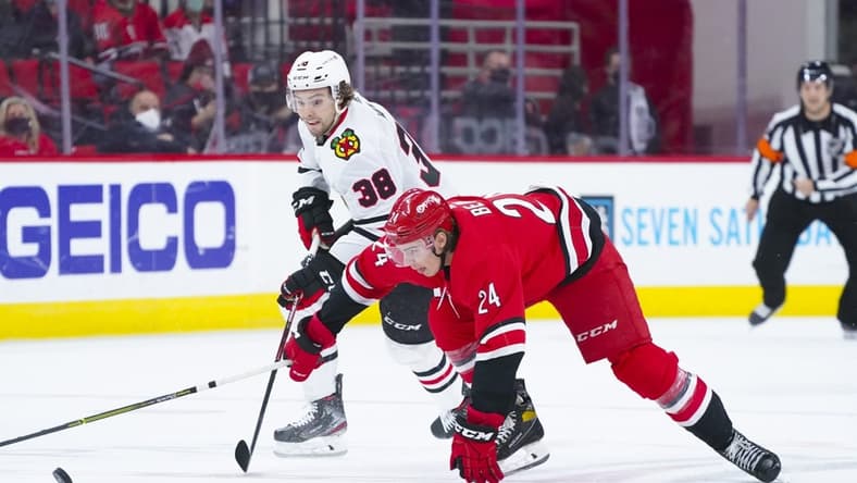 May 4, 2021; Raleigh, North Carolina, USA; Carolina Hurricanes defenseman Jake Bean (24) and Chicago Blackhawks left wing Brandon Hagel (38 battle for the puck during the first period at PNC Arena. Mandatory Credit: James Guillory-USA TODAY Sports