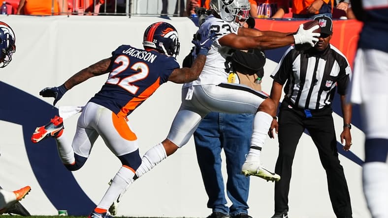 Oct 17, 2021; Denver, Colorado, USA; Las Vegas Raiders running back Kenyan Drake (23) leaps past Denver Broncos safety Kareem Jackson (22) to score a touchdown in the second quarter at Empower Field at Mile High. Mandatory Credit: Ron Chenoy-USA TODAY Sports