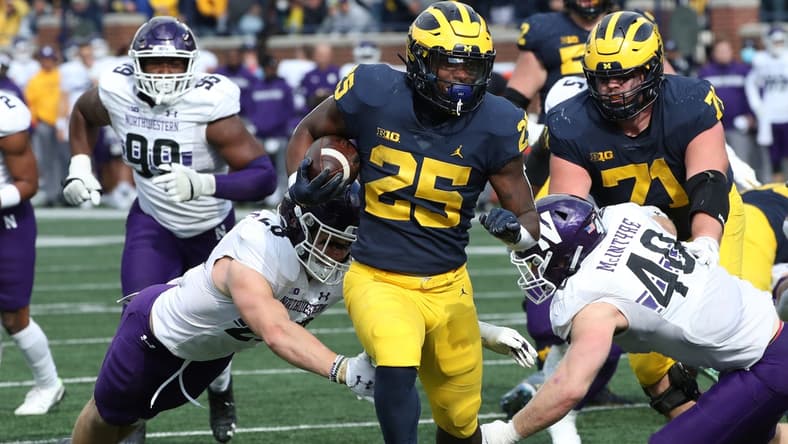 Michigan Wolverines running back Hassan Haskins (25) runs by Northwestern Wildcats defensive back Trent Carrington (20) and linebacker Peter McIntyre (40) during second half action Saturday, Oct. 23, 2021 at Michigan Stadium.

Mich Nw