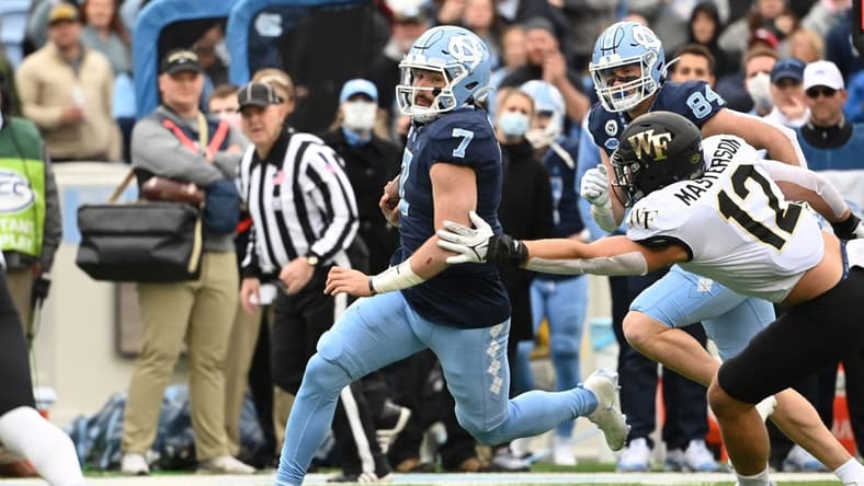 Nov 6, 2021; Chapel Hill, North Carolina, USA; North Carolina Tar Heels quarterback Sam Howell (7) runs as Wake Forest Demon Deacons defensive back Luke Masterson (12) defends in the first quarter at Kenan Memorial Stadium. Mandatory Credit: Bob Donnan-USA TODAY Sports