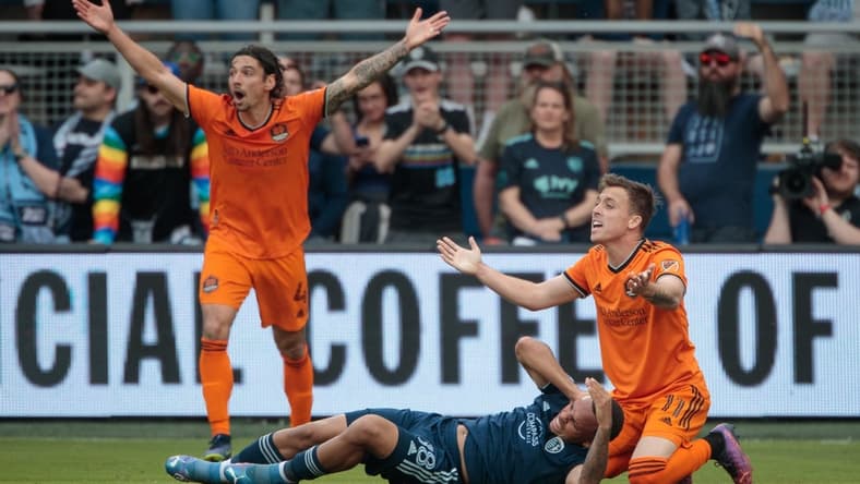 Mar 5, 2022; Kansas City, Kansas, USA; Houston Dynamo forward Corey Baird (11) and Houston Dynamo defender Zarek Valentin (4) react to a call after a collision with Sporting Kansas City defender Logan Ndenbe (18) at Children's Mercy Park. Mandatory Credit: William Purnell-USA TODAY Sports