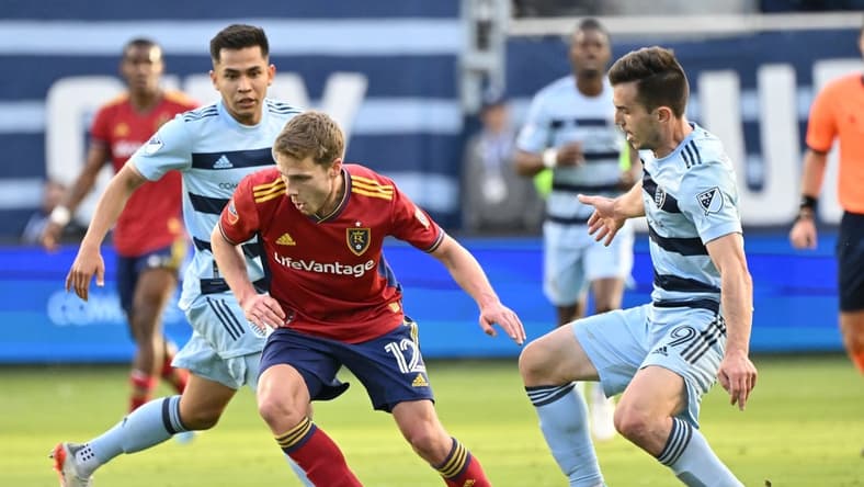 Mar 26, 2022; Kansas City, Kansas, USA;  Real Salt Lake midfielder Scott Caldwell (12) dribbles the ball against Sporting Kansas City forward Alan Pulido (9) during the first half at Children's Mercy Park. Mandatory Credit: Peter Aiken-USA TODAY Sports