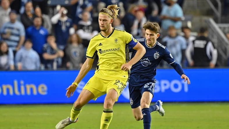 Apr 9, 2022; Kansas City, Kansas, USA; Nashville SC defender Walker Zimmerman (25) passes the ball while defended by Sporting Kansas City midfielder Marinos Tzionis (27) during the second half at Children's Mercy Park. Mandatory Credit: Peter Aiken-USA TODAY Sports
