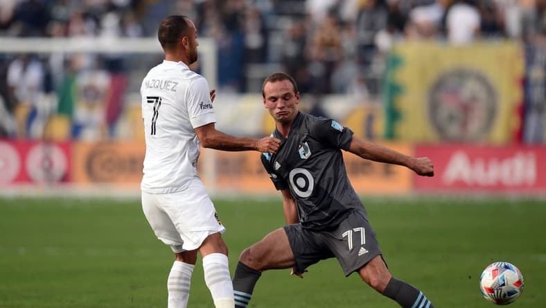 Nov 7, 2021; Carson, California, USA; Minnesota United defender Chase Gasper (77) and Los Angeles Galaxy midfielder Victor Vazquez (7) go for a loose ball during the first half at Dignity Health Sports Park. Mandatory Credit: Joe Camporeale-USA TODAY Sports