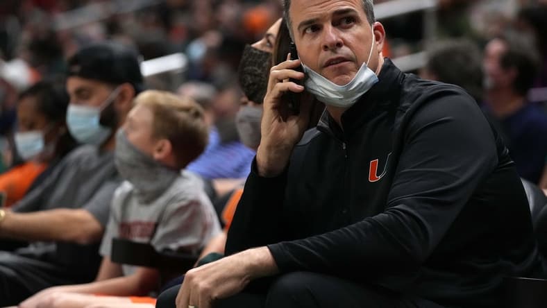 Feb 2, 2022; Coral Gables, Florida, USA; Miami Hurricanes head football coach Mario Cristobal talks on a phone while sitting court-side during the second half between the Miami Hurricanes and the Notre Dame Fighting Irish at Watsco Center. Mandatory Credit: Jasen Vinlove-USA TODAY Sports