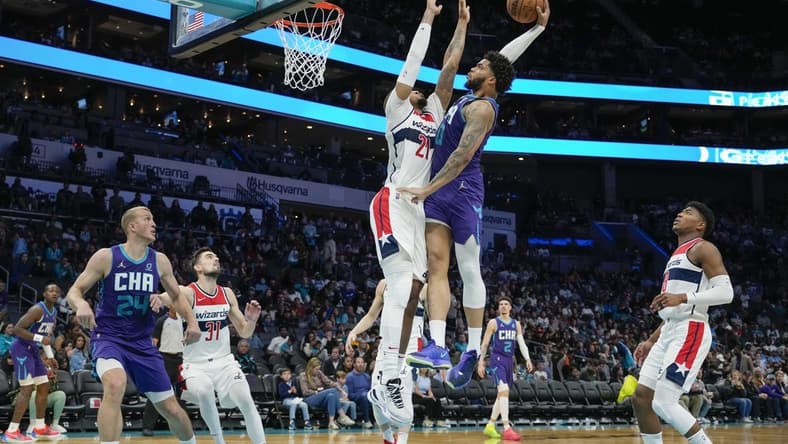 Apr 10, 2022; Charlotte, North Carolina, USA; Charlotte Hornets forward Miles Bridges (0) goes for the dunk defended by Washington Wizards center Daniel Gafford (21) during the second half at Spectrum Center. Mandatory Credit: Jim Dedmon-USA TODAY Sports