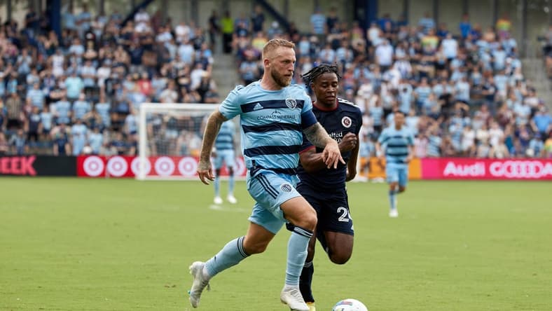 Jun 12, 2022; Kansas City, Kansas, USA; Sporting Kansas City forward Johnny Russell (7) running with the ball with New England Revolution forward DeJuan Jones (24) defending at Children's Mercy Park. Mandatory Credit: Gary Rohman-USA TODAY Sports