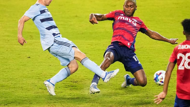 May 10, 2022; Kansas City, Kansas, USA; Sporting Kansas City forward Nikola Vujnovic (19) scores a goal against FC Dallas defender Nkosi Tafari (17) during the second half at Children's Mercy Park. Mandatory Credit: Jay Biggerstaff-USA TODAY Sports