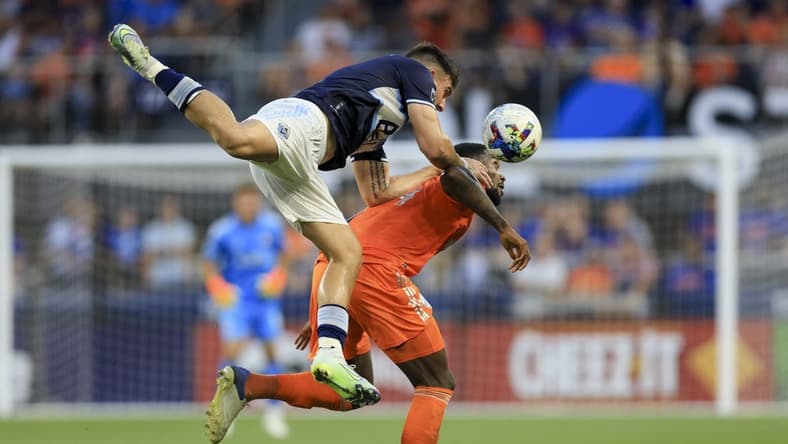 Jul 13, 2022; Cincinnati, Ohio, USA; Vancouver Whitecaps forward Lucas Cavallini (top) attempts to play the ball against FC Cincinnati defender Tyler Blackett (24) in the first half at TQL Stadium. Mandatory Credit: Aaron Doster-USA TODAY Sports