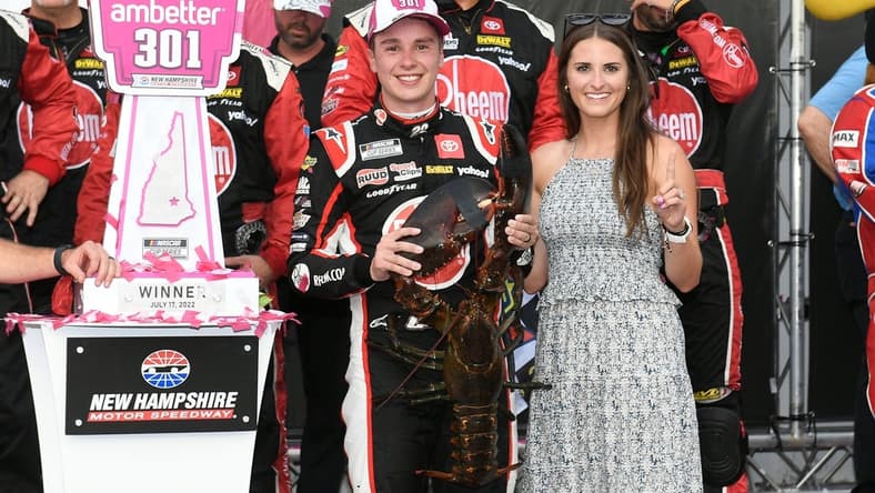 Jul 17, 2022; Loudon, New Hampshire, USA; NASCAR Cup Series driver Christopher Bell (20) and wife Morgan Kemenah celebrate on victory lane with Loudon the lobster after the Ambetter 301 at New Hampshire Motor Speedway. Mandatory Credit: Eric Canha-USA TODAY Sports
