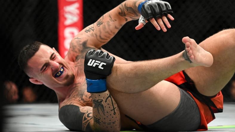 Jul 23, 2022; London, United Kingdom; Tom Aspinall (blue gloves) falls to the ground while fighting Curtis Blaydes during UFC Fight Night at O2 Arena. Mandatory Credit: Per Haljestam-USA TODAY Sports