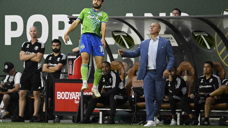 Aug 26, 2022; Portland, Oregon, USA; Seattle Sounders midfielder Alex Roldan (16) heads the ball during the first half next to Portland Timbers head coach Giovanni Savarese at Providence Park. The Timbers won 2-1. Mandatory Credit: Troy Wayrynen-USA TODAY Sports