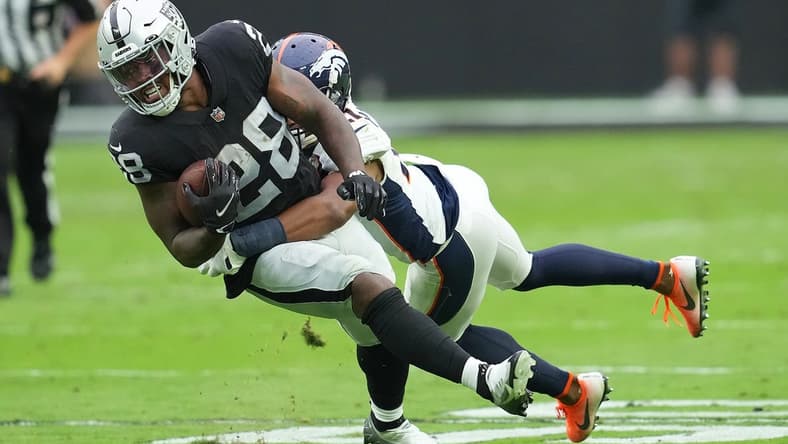 Oct 2, 2022; Paradise, Nevada, USA; Las Vegas Raiders running back Josh Jacobs (28) is tackled by Denver Broncos cornerback K'Waun Williams (21) during a game at Allegiant Stadium. Mandatory Credit: Stephen R. Sylvanie-USA TODAY Sports